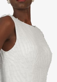 White dress with beaded embellishments, featuring a smooth texture and a fitted silhouette, accentuating curves and intricate detailing.