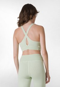 Ljusgrön sport-bh tillverkad av stretchigt material, med korsade axelremmar och en liten utskärning på baksidan. Matchande leggings synliga.