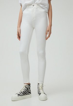 Close-up of person wearing tight white jeans and black-and-white zebra print high-top sneakers with thick soles.