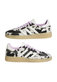 Pair madala säärega Adidas tossusid, millel on musta-valge lehmakujundusega muster, helelillad paelad, valged triibud ja läbipaistvad kummist tallad.