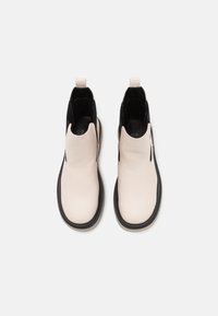 Light beige ankle boots with a smooth leather upper, black stretchy fabric sides, and a black rubber sole. Loop tab at the back for easy wear.