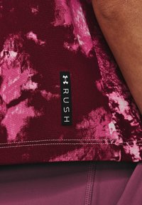 Atletická košile s tie-dye vzorem v barvách vínové a růžové, s šedým prošíváním a štítkem Under Armour označeným "RUSH" blízko lemu.