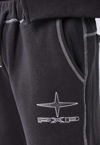 Pantalones de chándal gris oscuro con costuras en contraste blancas, bolsillo frontal, detalle de cremallera y logo "PXP" con estrella de cuatro puntas en el muslo.