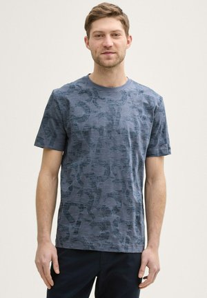 Short-sleeve navy blue t-shirt featuring a subtle graphic pattern, crew neck, and soft texture. Paired with dark pants.
