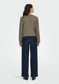 Brown houndstooth-patterned cropped blazer with gold button accents, paired with wide-leg dark denim jeans featuring visible stitching.