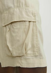 Shorts cargo beiges en tissu léger, dotés de grandes poches plissées, de coutures renforcées et d'une coupe décontractée.