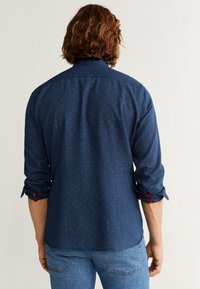 Camicia button-up blu scuro con piccoli dettagli a motivo, maniche arrotolate e contrasti rossi sui polsini. Vista posteriore mostrata.