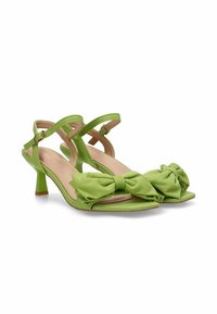Sandalias verdes de tacón con correa al tobillo, detalle de lazo en la punta. Textura suave, forma de punta afilada, tacón de altura media y plantilla en tono bronceado contrastante.