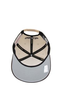 Gorra con visera gris, forro interior negro, tela beis y costuras decorativas. Incluye varios logotipos y una etiqueta de tamaño en el interior.