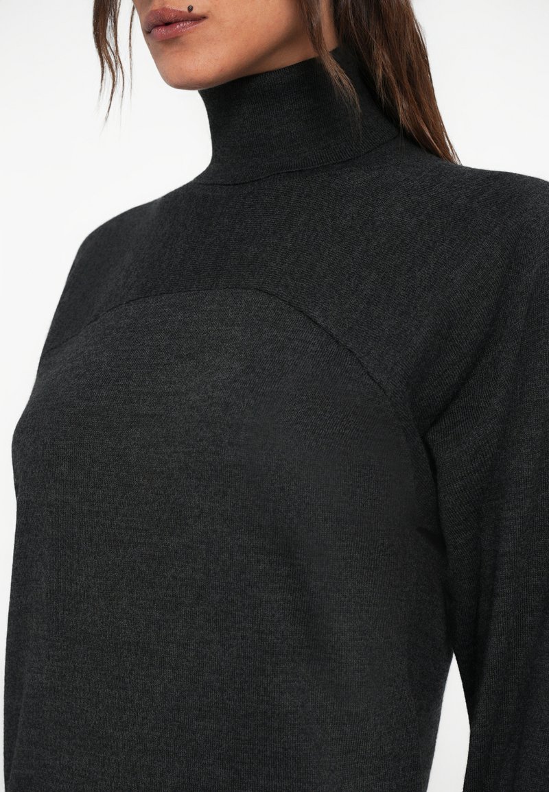 Mørkegrå turtleneck sweater lavet af et blødt strikket materiale, der har et sømløst design og en let struktureret overflade på frontpanelet.