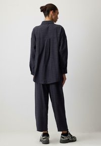 Oversized, dark gray checked shirt with long sleeves, lightweight fabric, paired with loose-fit matching pants and sporty black shoes.