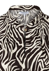 Schwarze und cremefarbene Bluse im Zebra-Print, mit Stehkragen, Knopfdetails und Falten, aus einem weichen, leichten Stoff gefertigt.