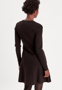 Dunkelbraunes, geripptes Strickkleid mit enganliegendem Oberteil und weit ausgestellt Rock mit vertikaler Nahtgestaltung. Lange Ärmel mit gerippten Bündchen.