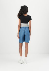 Black short-sleeve top with a grey waistband, paired with blue denim shorts featuring an elastic waist and two back pockets. White sneakers worn.