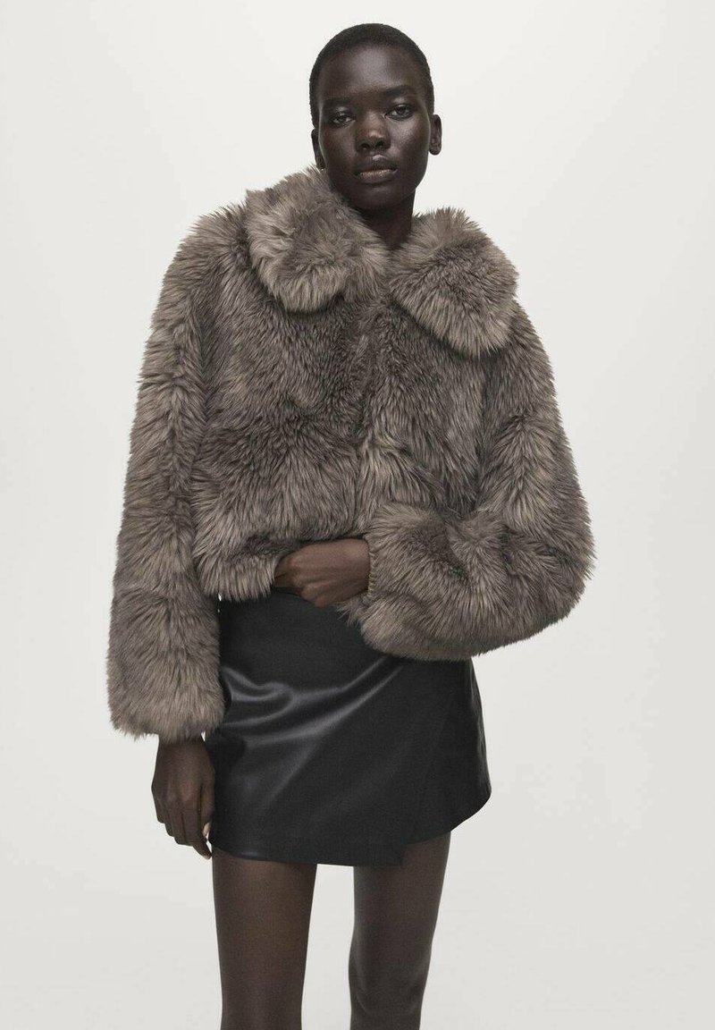 Krótkie futrzane kurtka z imitacji futra w jasnobrązowym kolorze z szerokim kołnierzem i długimi rękawami, zestawiona z obcisłą czarną mini spódnicą. Gładka tekstura i puszysty wygląd.