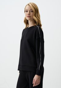 Zwarte sweatshirt met een relaxed fit, voorzien van witte zijstrepen en een ronde halslijn. Soepele textuur, lange mouwen en taps toelopende manchetten.