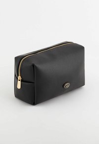 Pochette noire texturée avec fermeture éclair dorée, présentant une forme arrondie et un petit logo sur le devant. Design compact et angulaire.