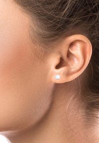Boucle d'oreille en argent avec une forme circulaire lisse. Positionnée sur une oreille lobée, réfléchissant la lumière grâce à une finition polie. Design subtil et minimaliste.