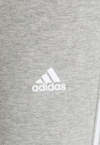 Pantaloni sportivi grigi realizzati in tessuto morbido. Presentano un logo Adidas bianco e una superficie texturizzata. Design semplice, privo di ulteriori motivi.