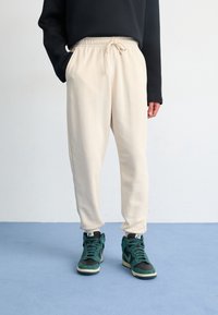 Krémové tepláky s elastickým pasem a šňůrkou, s bočními kapsami. Spárovány s černými a tyrkysovými vysokými teniskami.