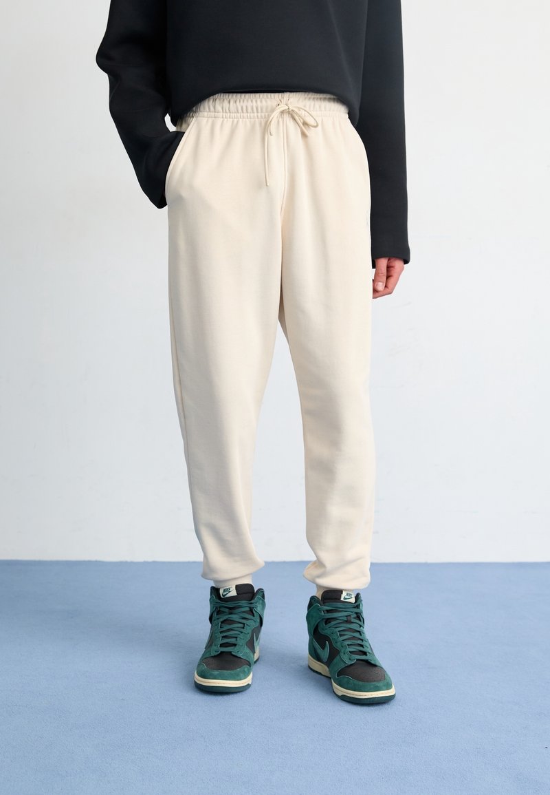 Krémové tepláky s elastickým pasem a šňůrkou, s bočními kapsami. Spárovány s černými a tyrkysovými vysokými teniskami.