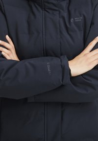 Námornícky modrá zateplená bunda s vysokým golierom, prešitými detailmi a logom "North Bend"; látka má hladký a odolný povrch.