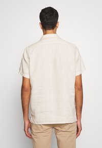 Camicia di lino beige a maniche corte con colletto, caratterizzata da una vestibilità comoda e una texture sottile. La vista posteriore mostra cuciture pulite e dettagli dell'orlo.