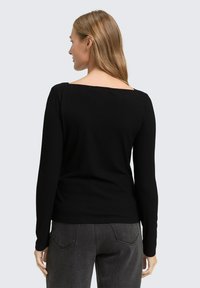 Zwarte geribbelde lange mouw top met een vierkante halslijn, heeft een aansluitend ontwerp en een zachte textuur. Gepaard met grijze jeans, gezien vanuit de achterkant.