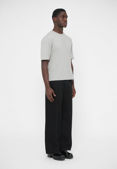 Sivá tričko s krátkym rukávom a okrúhlym výstrihom, nosené s čiernymi vysokými nohavicami a čiernymi platformovými topánkami. Hladká textúra látky.