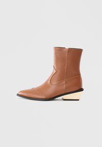 Botină din piele maro până la gleznă, cu vârf ascu�țit, detaliu cu cusătură pe lateral curbată și un toc unghiular bej unic. Textură netedă, design minimalist.