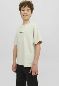 Ljusbeige bomullströja med korta ärmar och rund halsringning. Har "Originals Studio" tryckt i svart på framsidan.