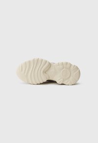 Shoe sole in cream, featuring a wavy pattern with deep grooves for traction. Durable rubber material with a rounded shape and embossed logo.