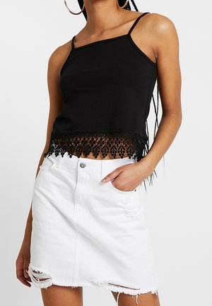 Sort ærmeløs crop top med blonderkant i kanten, parret med en hvid denimnederdel med slid og frynsede kanter.