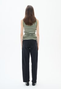 Zelený žebrovaný top bez rukávů spárovaný s černými širokými kalhotami s vysokým pasem. Outfit má jednoduchý design s čistými liniemi.