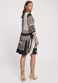 Czarna i biała sukienka w paski z beżowymi akcentami, z dopasowanym gorsetem, rękawami do łokcia i wielowarstwową spódnicą. Gładka tekstura materiału.