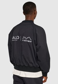 Czarna kurtka bombka z żeberkowymi mankietami i dołem, z białym nadrukowanym tekstem i wzorem z tyłu. Wykonana z gładkiego, lekkiego materiału.