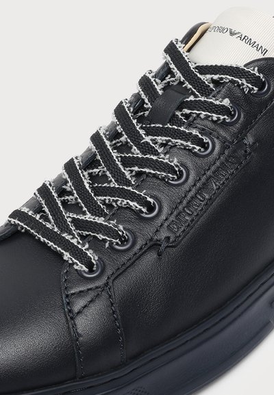 Baskets en cuir noir avec lacets texturés noirs et blancs, détails cousus et logo "Emporio Armani" sur le côté et la languette.
