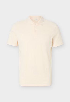 Polo manches courtes de couleur crème avec patte à deux boutons et col classique sur un fond neutre.
