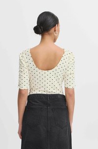Top a righe bianco con pois, maniche corte e scollatura profonda sulla schiena, abbinato a una gonna in denim nera a vita alta con tasche posteriori.
