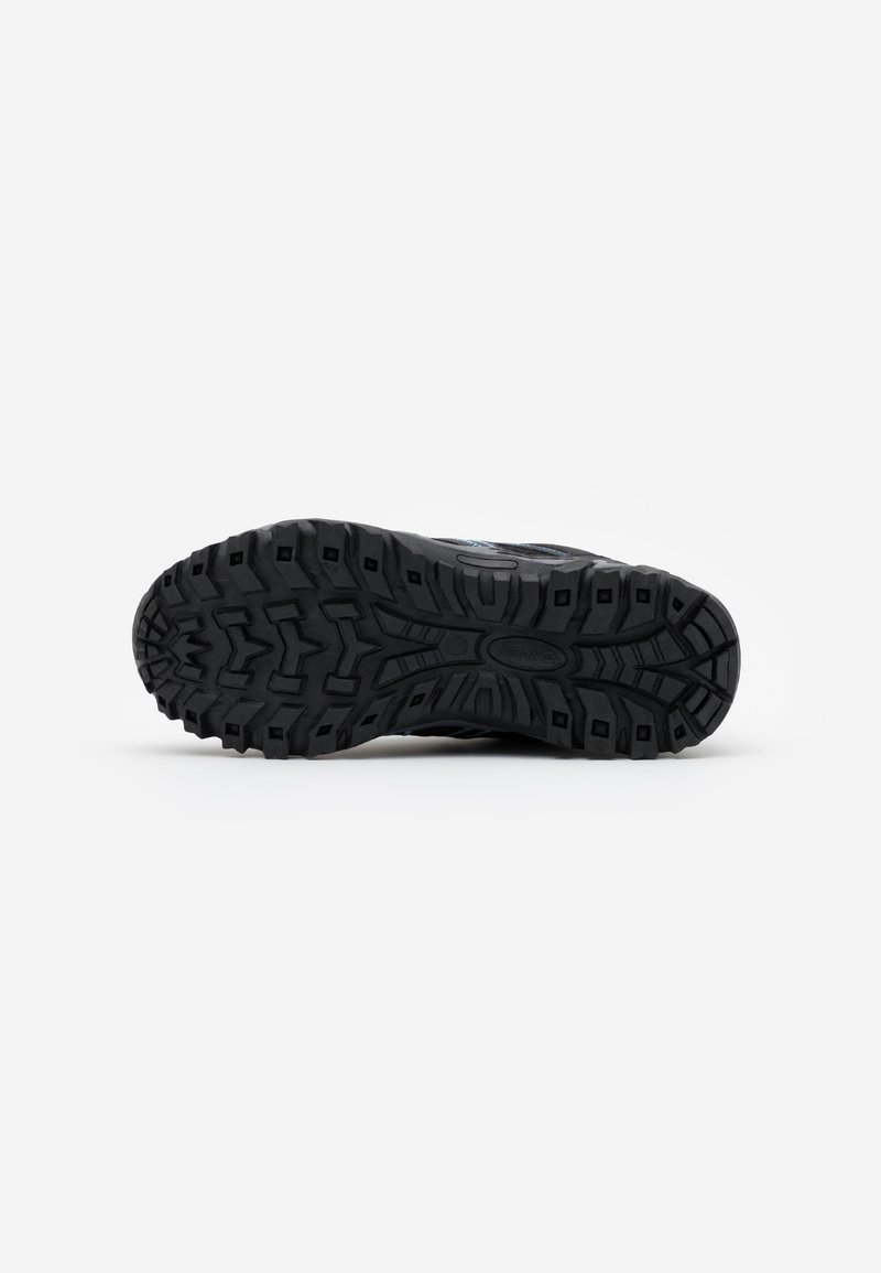 Suela de zapatilla deportiva negra con un patrón de banda de rodadura rugoso para tracción, con un tacón ligeramente elevado y material de goma texturizada.