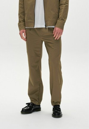 Pantalones marrones, ligeros y ajustados, con una textura suave y puños elásticos, llevados con zapatos negros con un detalle de flecos.
