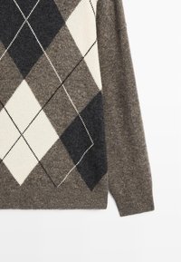 Maglione di lana marrone con un grande motivo argyle in nero, bianco e grigio che copre la parte anteriore, mostrando la manica e il lato.