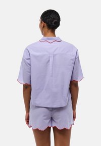 Ensemble de pyjama lilas composé d'un haut à col et à manches courtes avec des bords en forme de coquille rouges et d'un short assorti avec des ourlets en forme de coquille. Tissu en coton.