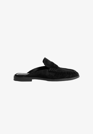 Sorte ruskinds slip-on loafers med lav profil, der har syninger på overdelen og en flad gummisål.