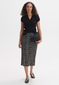Top corto a maniche corte nero a costine abbinato a una gonna midi con motivo in bianco e nero. Gli accessori includono una pochette nera trapuntata e scarpe flat.