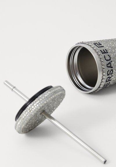 Metal drink tumbler covered in clear rhinestones, with a silver-colored straw and a black silicone ring on the lid. Features a sleek design.