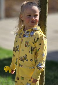 Gul zip-up hoodie och matchande byxor med lekfulla djurillustrationer, tillverkade av mjukt tyg, med detaljerade mönster och tassavtryck.