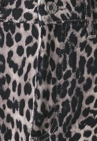 Tela de leopardo con manchas negras sobre un fondo beige claro, mezclilla texturizada con costuras visibles y un detalle de botón plateado.