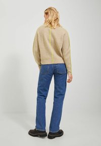 Maglione beige a coste con una striscia gialla sul retro, abbinato a jeans di denim blu e stivali neri chunky. Vista che mostra il retro dell'outfit.