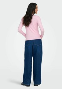 Langsleeve roze top gecombineerd met losse, donkerblauwe spijkerbroeken. Glad materiaal, ronde halslijn en een eenvoudig ontwerp zonder patronen.